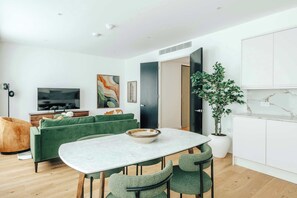 A modern living room with a green sofa, a dining table with chairs, a TV, and a large potted plant. - Luxury 2BR Apartment in Mayfair (London)
