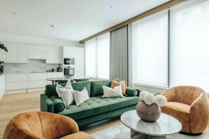 Ein modernes Wohnzimmer mit einem grünen Sofa, zwei Sesseln und einem Couchtisch aus Marmor.