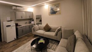 Una sala de estar moderna con sofá, mesa de centro y área de cocina con armarios y electrodomésticos.
