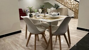 Un comedor con una mesa preparada para dos, sillas blancas y una escalera al fondo.