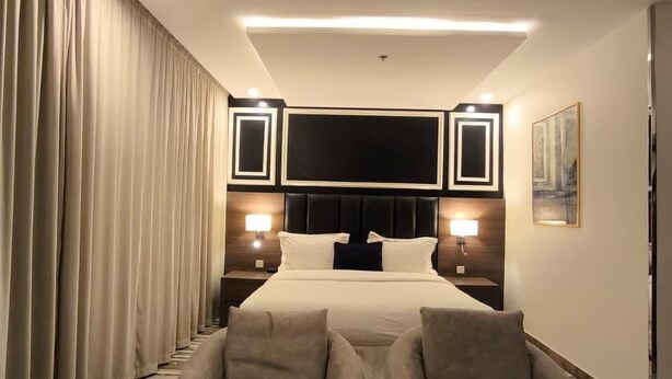 Un dormitorio de hotel con una cama, dos sillones, una mesita, un televisor y un cuadro en la pared.