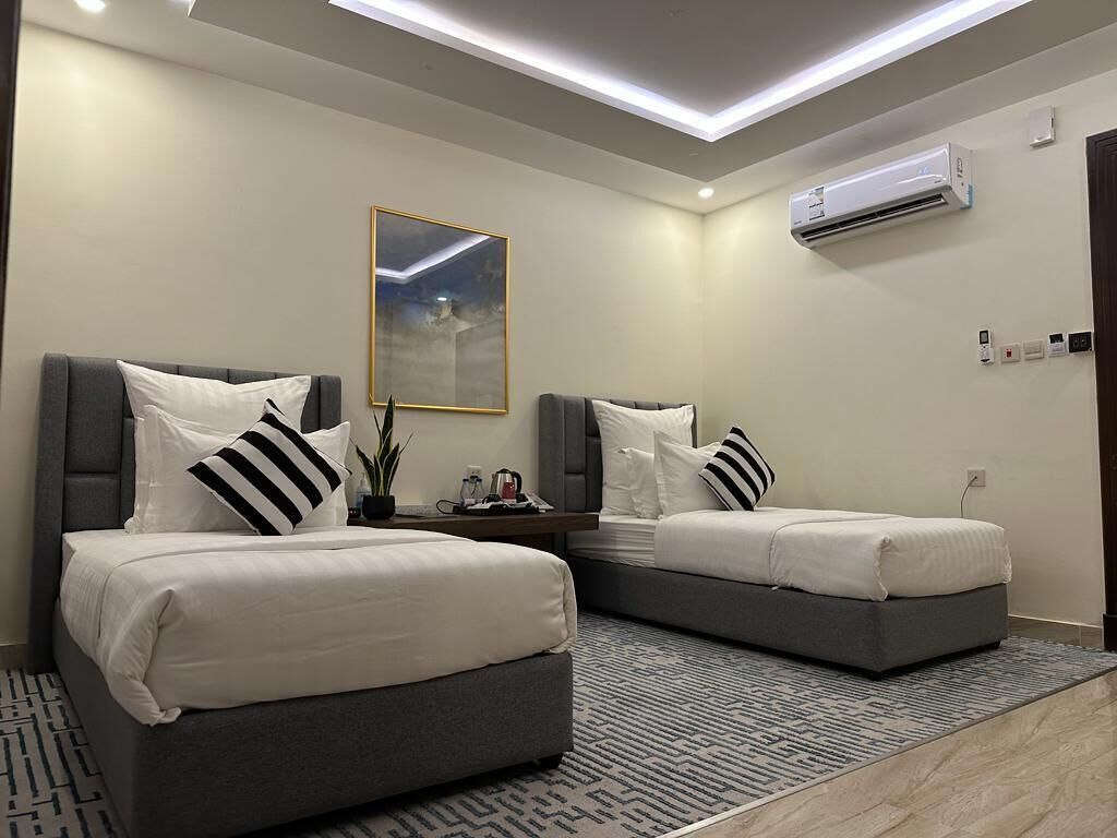 A modern hotel room with two beds, a ceiling light, an air conditioner, and a framed picture on the wall.
