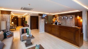 Un vestíbulo de hotel con mostrador de recepción, televisión y zona de estar con sofá y mesa de centro.