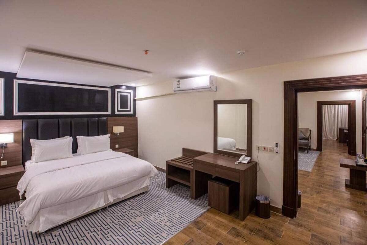 A hotel room with a bed, a desk, a mirror, and a bathroom visible through an open door.