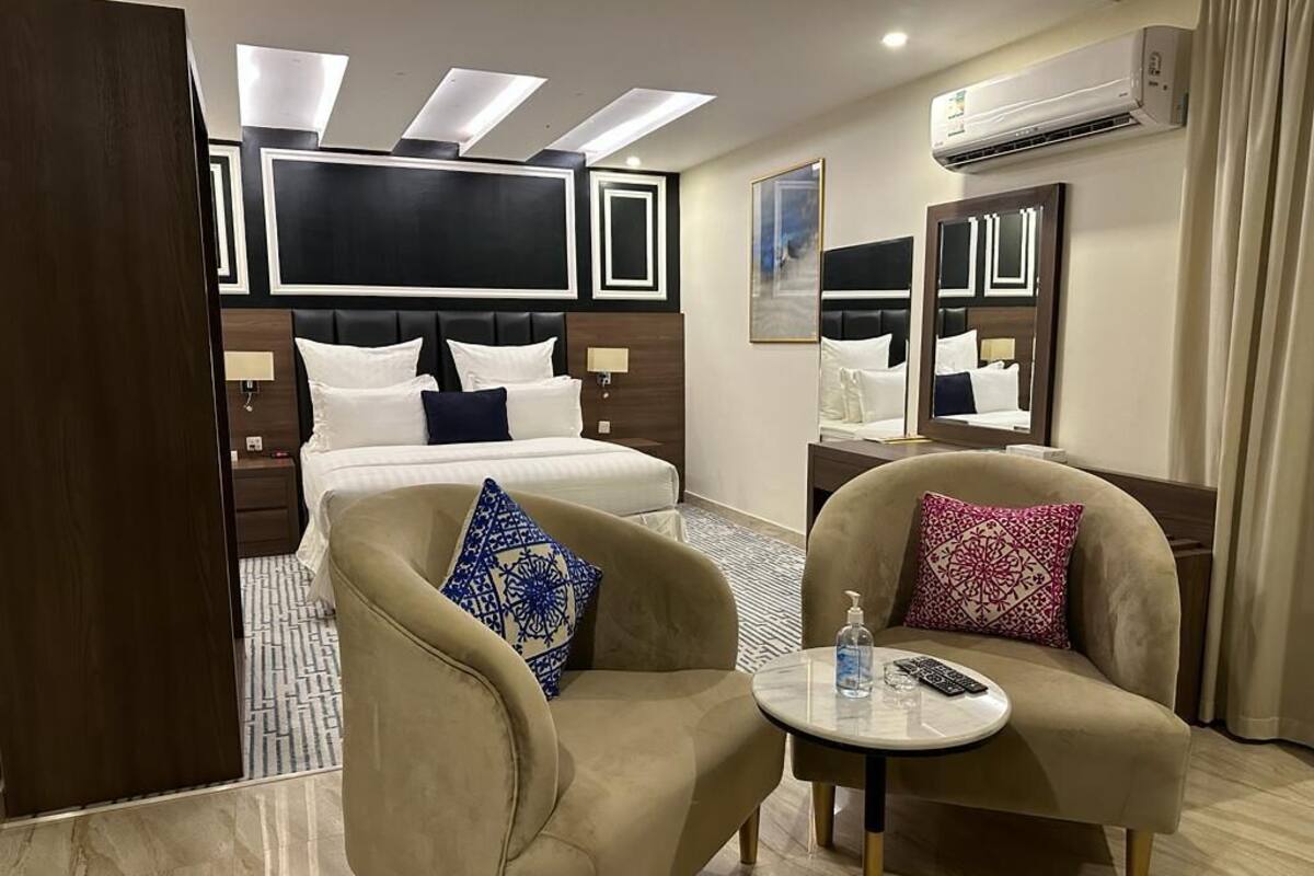 A hotel room with a bed, two armchairs, a small round table, and a large mirror.