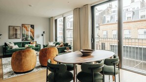 Ein modernes Wohnzimmer mit einem grünen Sofagarnitur, einem Holztisch und einem Essbereich mit Stühlen.