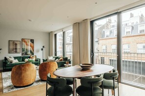 Ein modernes Wohnzimmer mit einem grünen Sofagarnitur, einem Holztisch und einem Essbereich mit Stühlen.