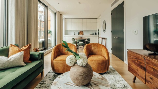 Ein modernes Wohnzimmer mit einem grünen Sofa, zwei orangefarbenen Sesseln, einer Holzkommode und einem Marmor-Couchtisch.