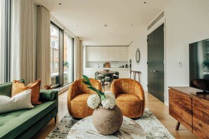 A modern living room with a green sofa, two orange armchairs, a wooden cabinet, and a marble coffee table. - Exquisite 2BD apartment in prestigious Mayfair (London)