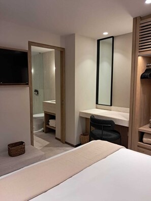 Una habitació d'hotel amb llit, escriptori, cadira, mirall i televisió.