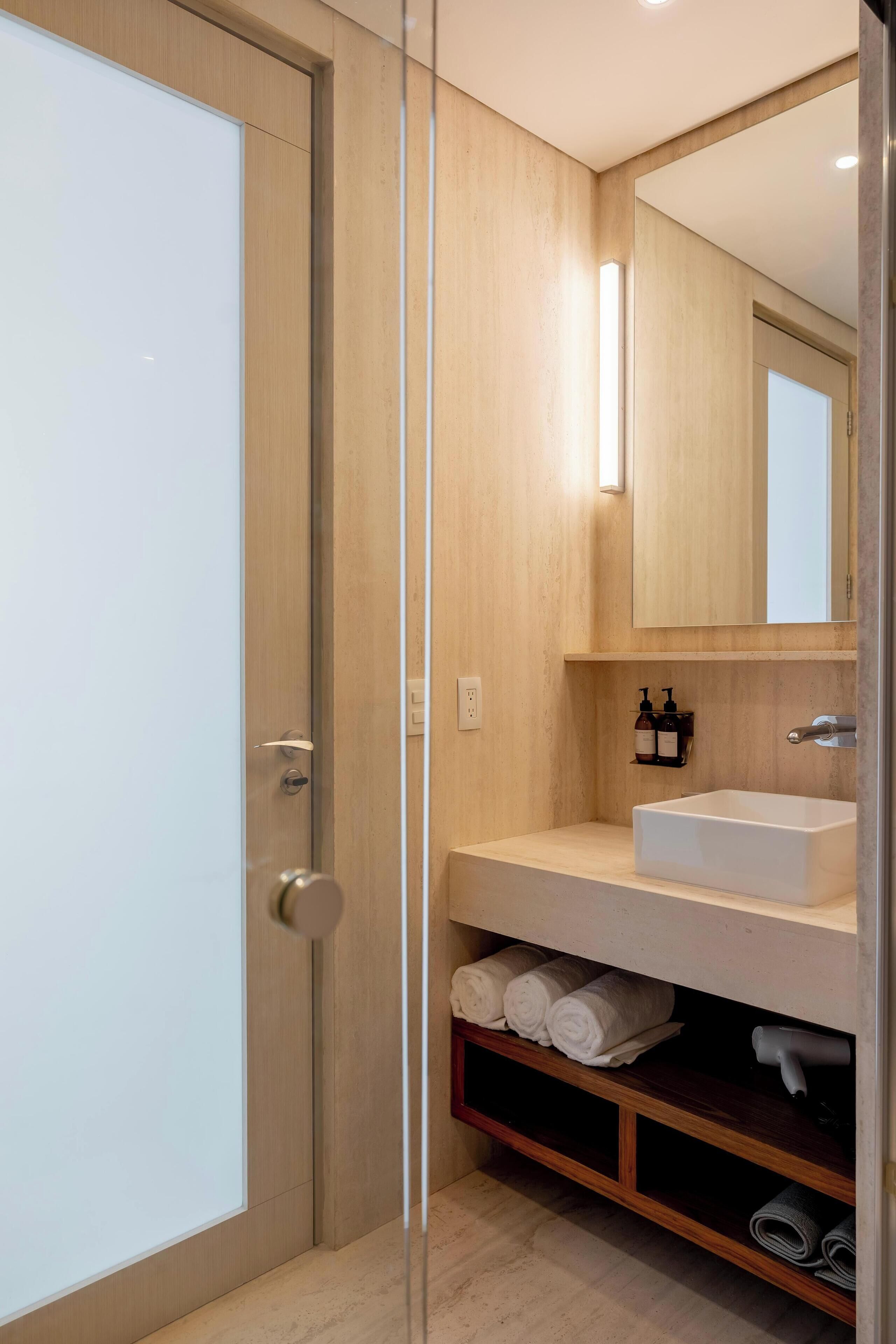 A modern bathroom with a wooden vanity, a white sink, and a mirror above it.