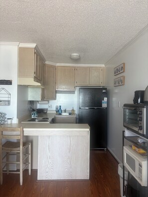 A kitchen with wooden cabinets, a black refrigerator, a microwave, and a toaster oven. - Welcome to Pellom's Perch. A Beautiful Oceanfront Couple's Retreat. (North Topsail Beach)