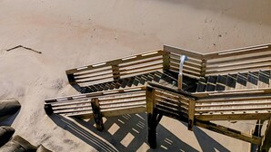 Une plage avec des chaises longues en bois et une promenade en béton qui mène à l’eau.