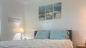 Une chambre à coucher comprenant un lit, une table de chevet, une lampe, une œuvre d’art accrochée au mur et un panneau affichant une citation inspirante.