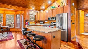 Une cuisine rustique, située dans une cabane en bois, avec un îlot central, des tabourets de bar, un réfrigérateur, un four à micro-ondes et une cuisinière.