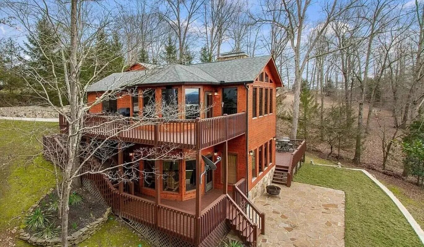A two-story log cabin with a balcony and a stone patio.