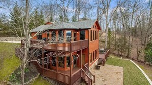 Une cabane en rondins à deux étages, dotée d’un balcon et d’une terrasse en pierre.