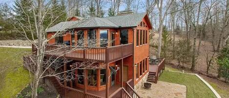 A two-story log cabin with a balcony and a stone patio.