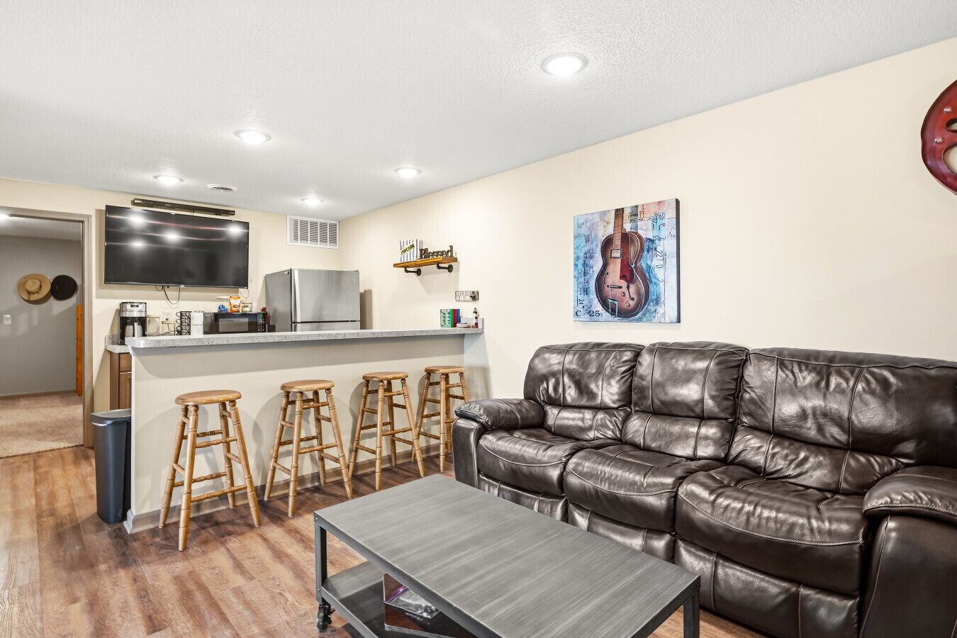A living room with a leather sofa, a coffee table, and a kitchen area with a refrigerator, stove, and bar stools.