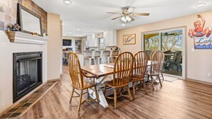 A dining area with a fireplace, wooden chairs, a ceiling fan, and a kitchen in the background. - The Hideaway: Large (7BD), Modern, Lakeview, Slip (LaFollette)