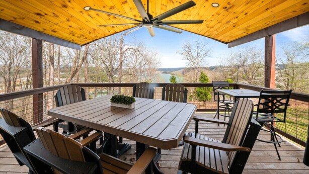 A covered outdoor deck with a table and chairs, a ceiling fan, and a view of a lake and trees. - The Hideaway: Large (7BD), Modern, Lakeview, Slip (LaFollette)