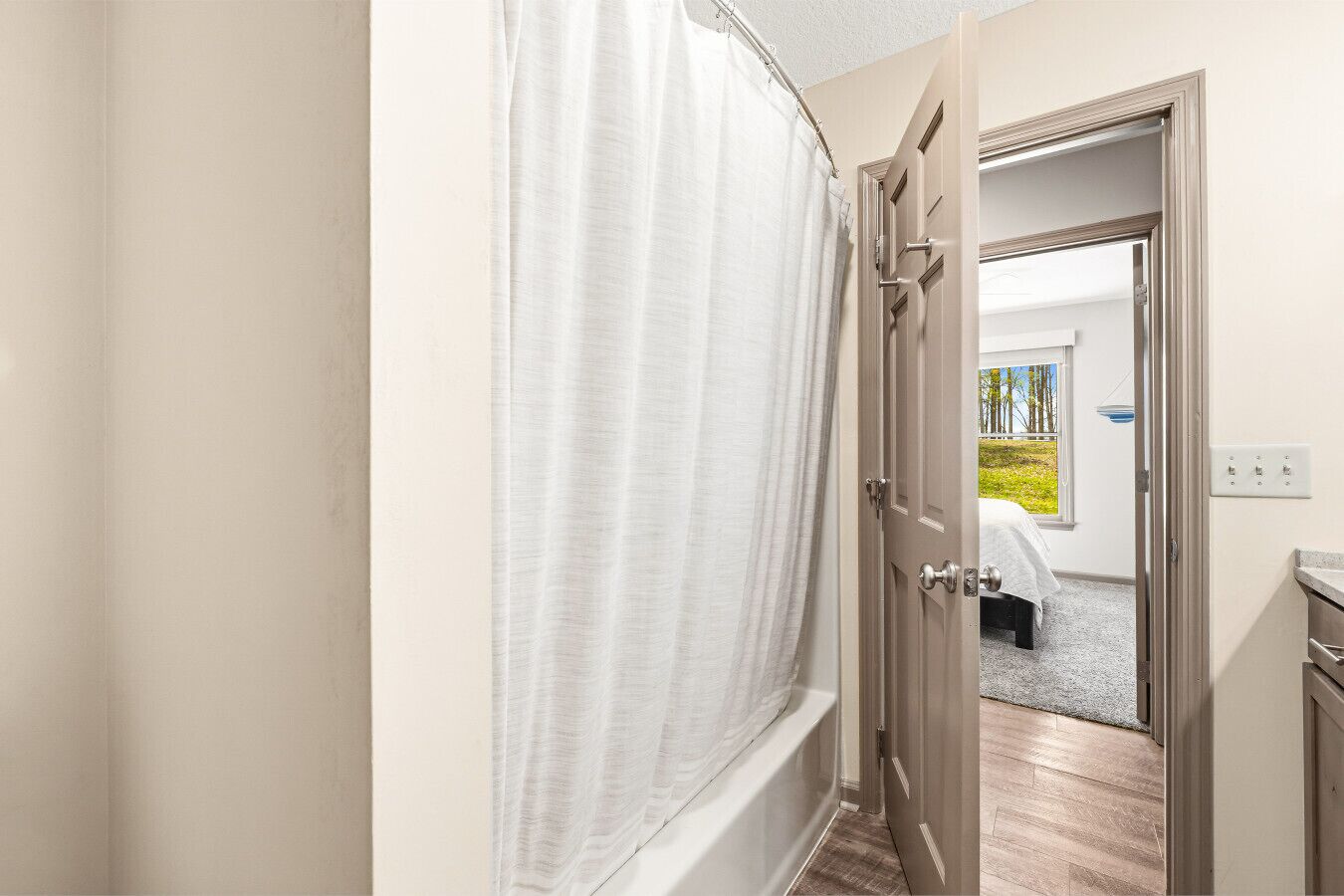 Habitación de hotel con cortina de ducha, puerta que da a un balcón y un taburete pequeño.