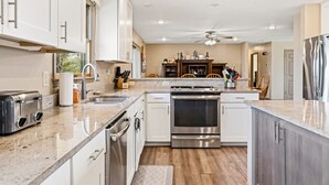 A modern kitchen with white cabinets, stainless steel appliances, a granite countertop, and a ceiling fan. - The Hideaway: Large (7BD), Modern, Lakeview, Slip (LaFollette)
