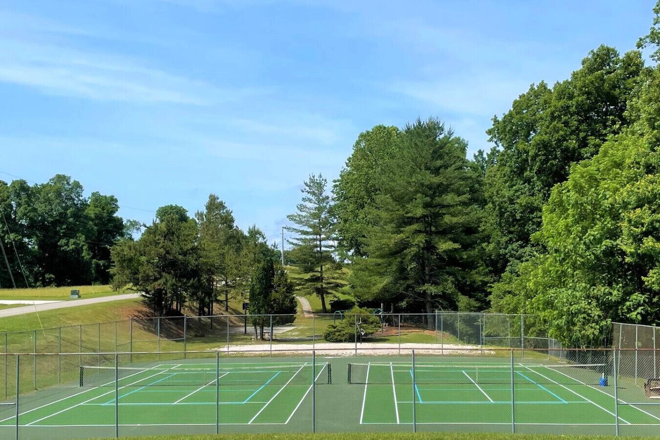 An outdoor tennis court surrounded by trees and a fence.
