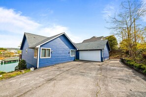 A two-story blue house with a garage, a driveway, and a body of water in the background.