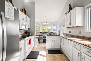 A modern kitchen with white cabinets, a black countertop, and a dining area with chairs.