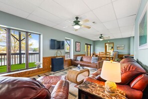 A spacious living room with a large window, a ceiling fan, a television, and a dining area.
