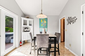 A dining area with a table, chairs, a pendant light, a decorative wall piece, and a white cabinet with shelves.