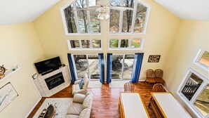 A spacious living room with a fireplace, a television, and a large window overlooking a deck. - Livin` the Dream: Lakefront, Dock, Firepit, 16 (LaFollette)