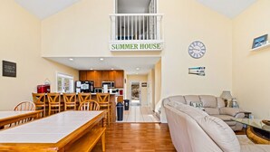 A spacious living area with a dining table, chairs, a sofa, and a balcony with a 'SUMMER HOUSE' sign. - Livin` the Dream: Lakefront, Dock, Firepit, 16 (LaFollette)