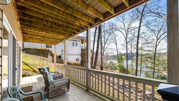 A covered porch with wicker chairs, a wooden deck, and a view of a lake and buildings. - Livin` the Dream: Lakefront, Dock, Firepit, 16 (LaFollette)