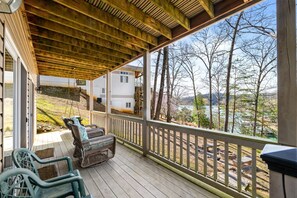 A covered porch with wicker chairs, a wooden deck, and a view of a lake and buildings. - Livin` the Dream: Lakefront, Dock, Firepit, 16 (LaFollette)