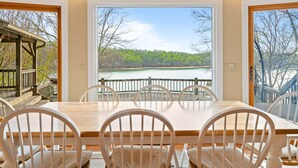 A dining area with a large table and chairs, a view of a lake, and a deck with a railing. - Poolside Paradise: Lakefront; Private Pool; Dock (LaFollette)