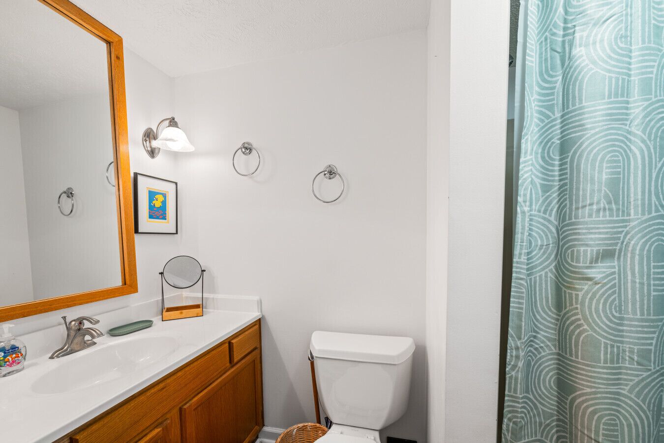 A bathroom with a white sink, mirror, and toilet, with a towel rack and a framed picture on the wall.