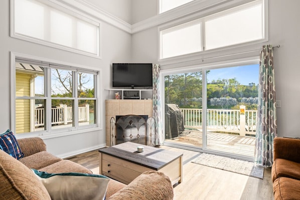 A spacious living room with a fireplace, large windows, and a view of a deck and greenery.
