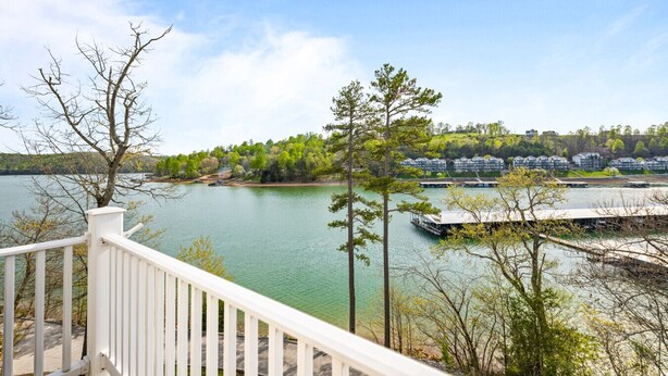 A lake with a dock, trees, and a row of buildings in the background.