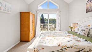 A bedroom with a large bed, a wardrobe, a ceiling fan, and a view of the outdoors.