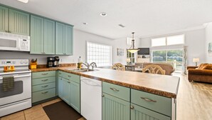 A modern kitchen with teal cabinetry, a central island, and a dining area with a view.