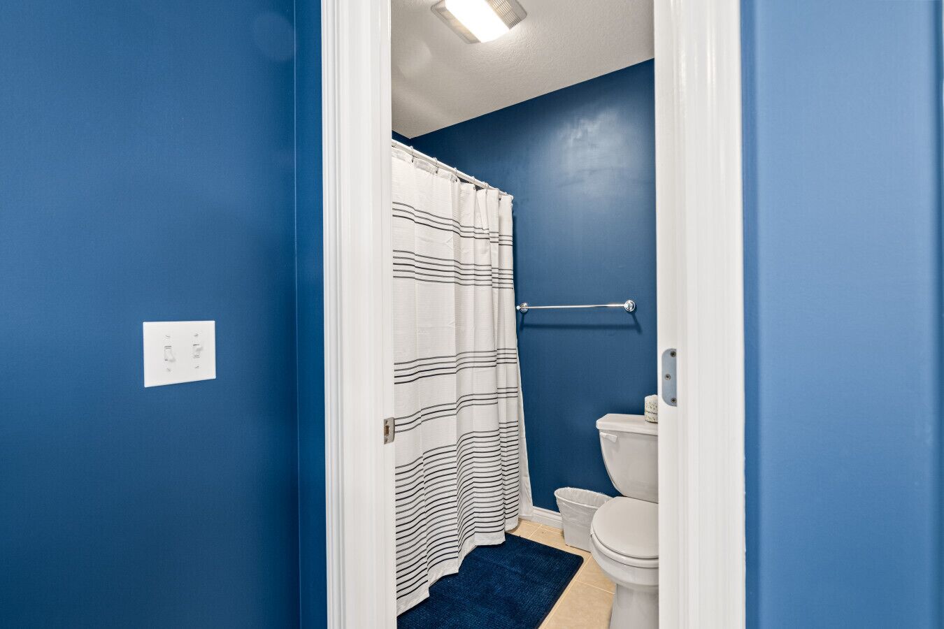 Une salle de bain avec des murs bleus, des toilettes blanches, un rideau de douche à rayures et un tapis bleu.