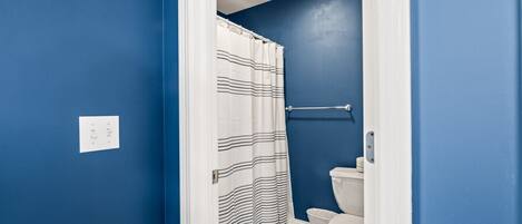 Une salle de bain avec des murs bleus, des toilettes blanches, un rideau de douche à rayures et un tapis bleu.