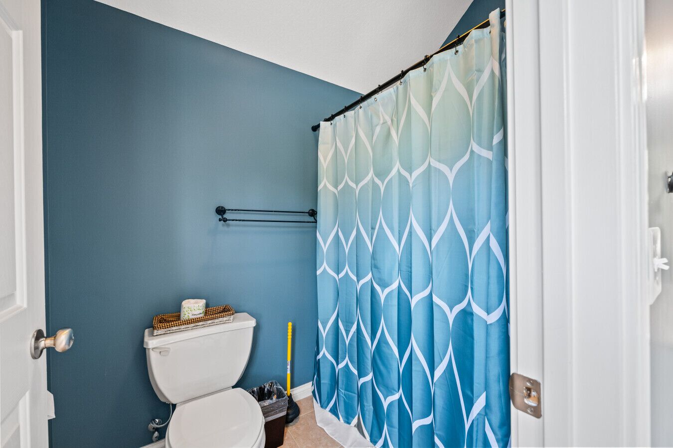 Een badkamer met een blauwe wand, een wit toilet, een douchegordijn met een geometrisch patroon, en een handdoekhouder.