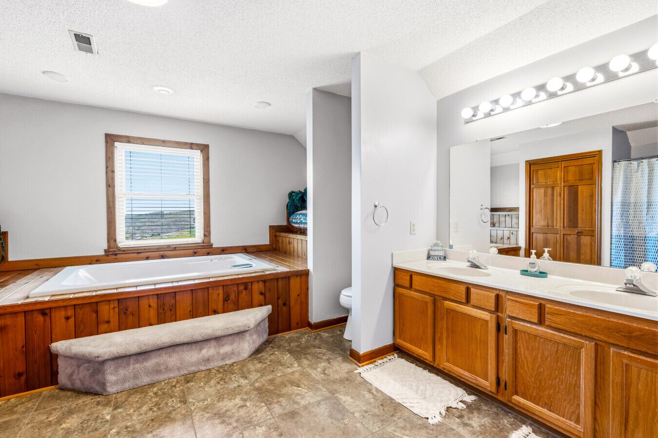 A bathroom with a bathtub, a large mirror, wooden cabinets, and a bench.