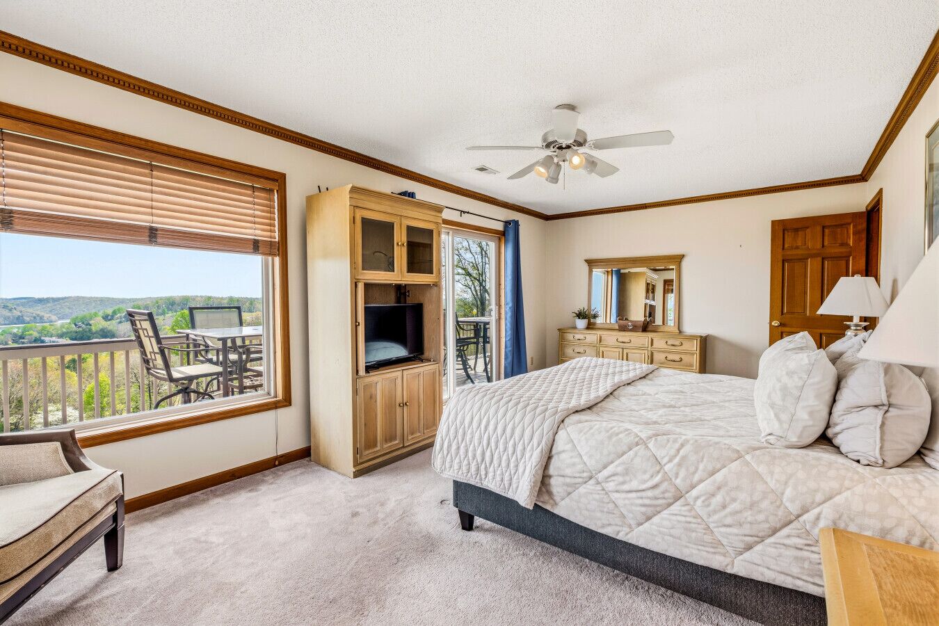 Une chambre à coucher comprenant un lit, une commode, un miroir, un ventilateur de plafond et un balcon avec une chaise et une table.