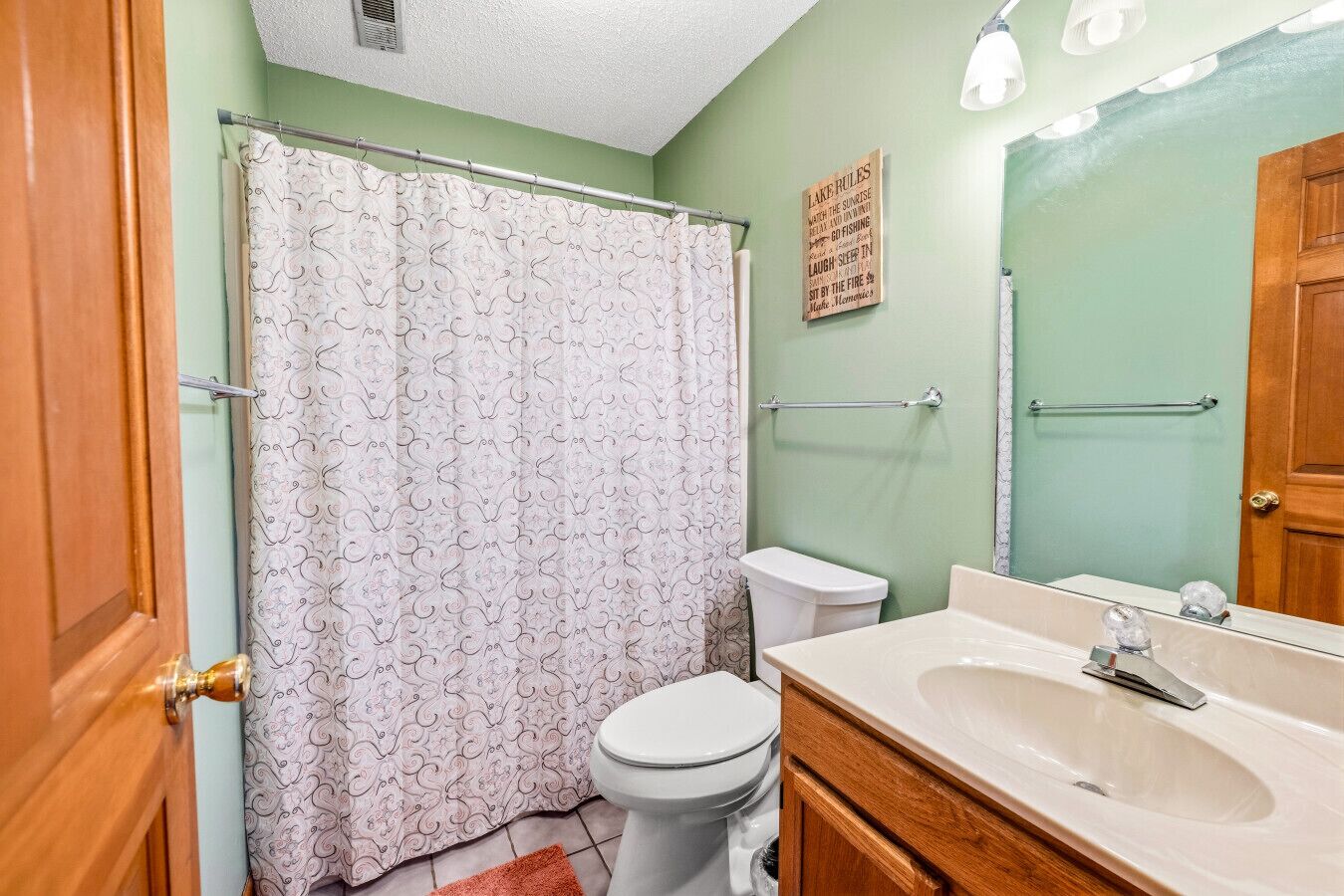 A bathroom with a shower curtain, toilet, sink, and mirror.
