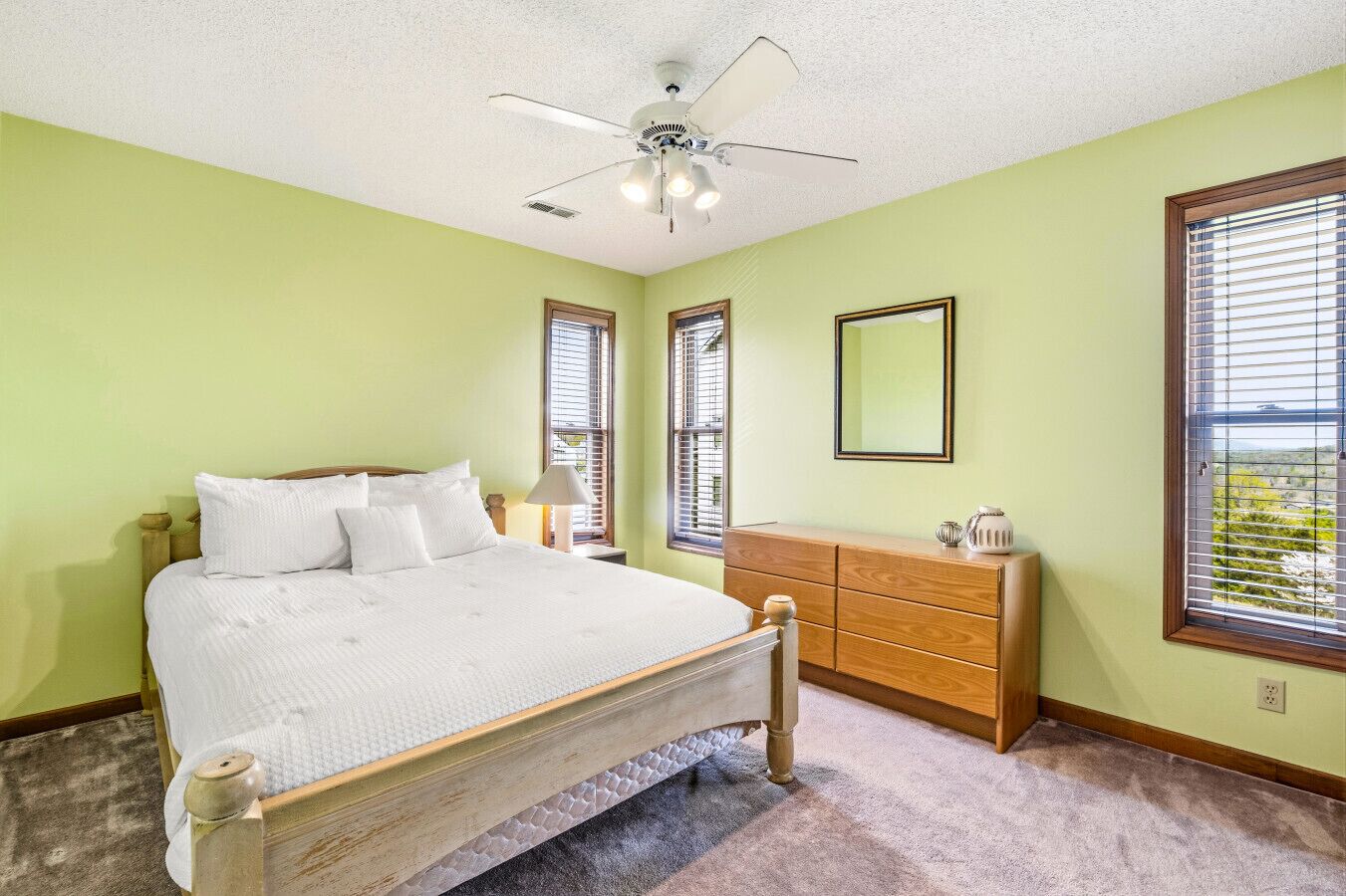 A bedroom with a bed, dresser, ceiling fan, and windows.