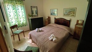 Ein Schlafzimmer mit einem Bett, einem Sessel, einem Schreibtisch, einem Spiegel und zwei Bildern an der Wand.